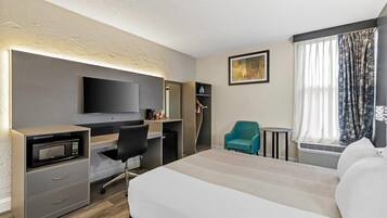 Habitación de hotel con cama, escritorio con computadora, microondas, silla, televisión y ventana con cortinas.