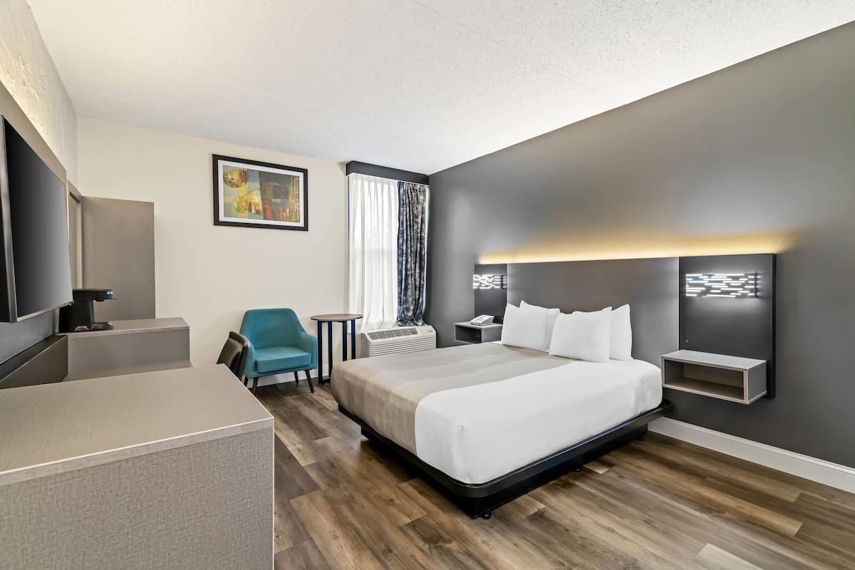 A modern hotel room with a large bed, a desk, a chair, and a TV.