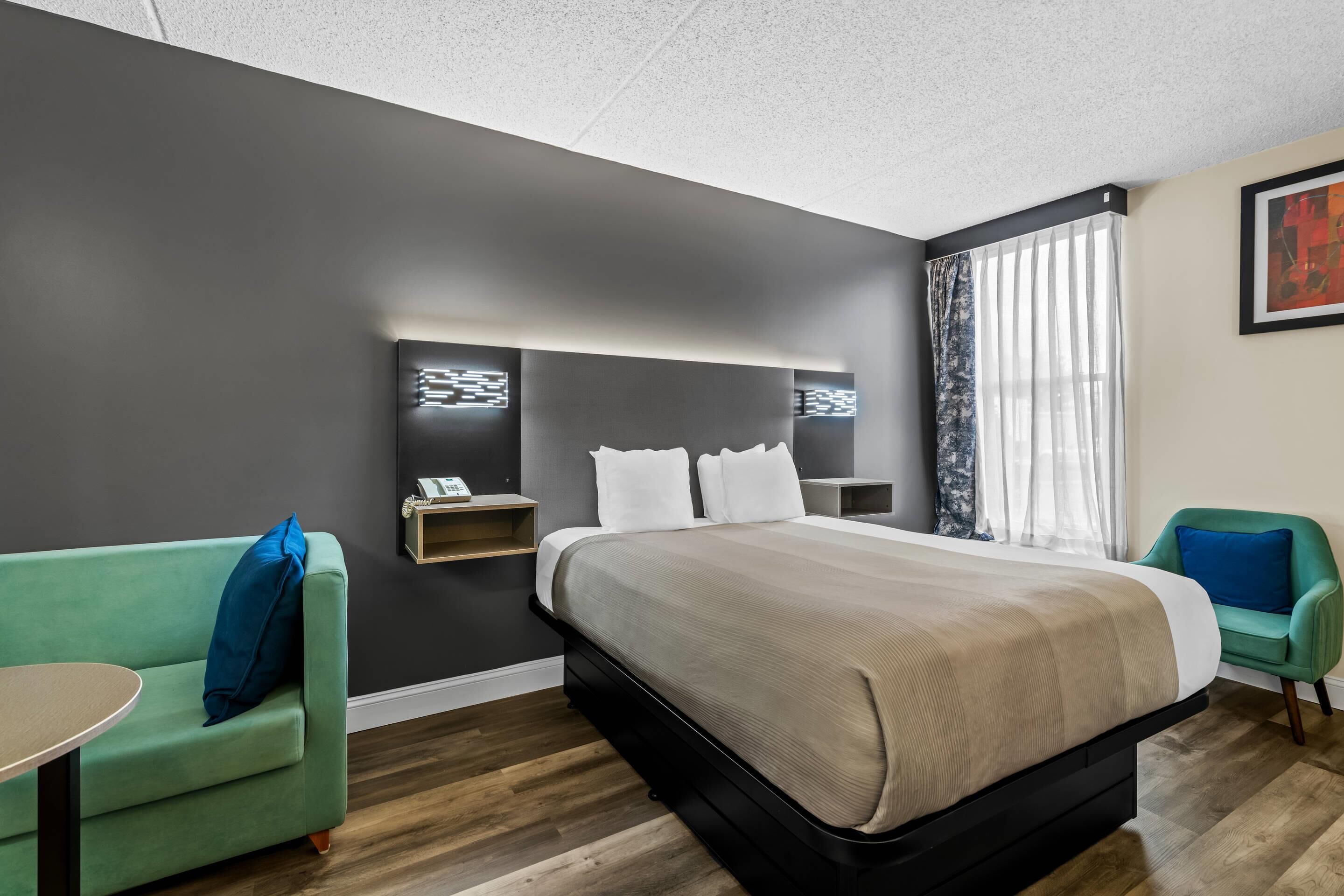 Ein modernes Hotelzimmer mit einem großen Bett, einem grünen Sofa, einem kleinen Tisch und einem Fenster mit transparenten Vorhängen.