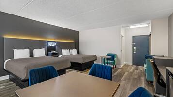 A hotel room with two beds, a desk, a chair, and a small table.