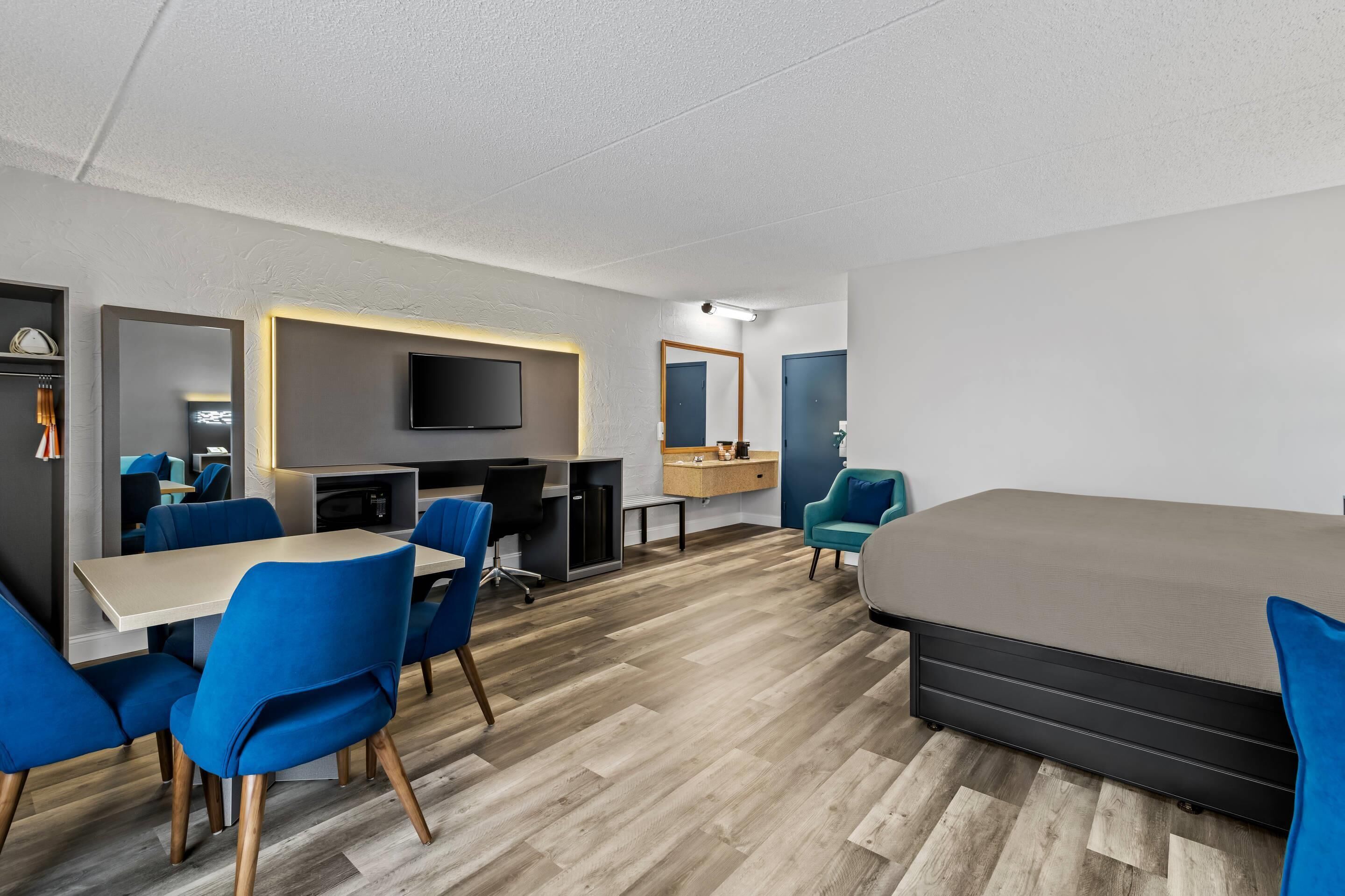 A modern hotel room with a large bed, a desk with a chair, a TV, and a mirror.