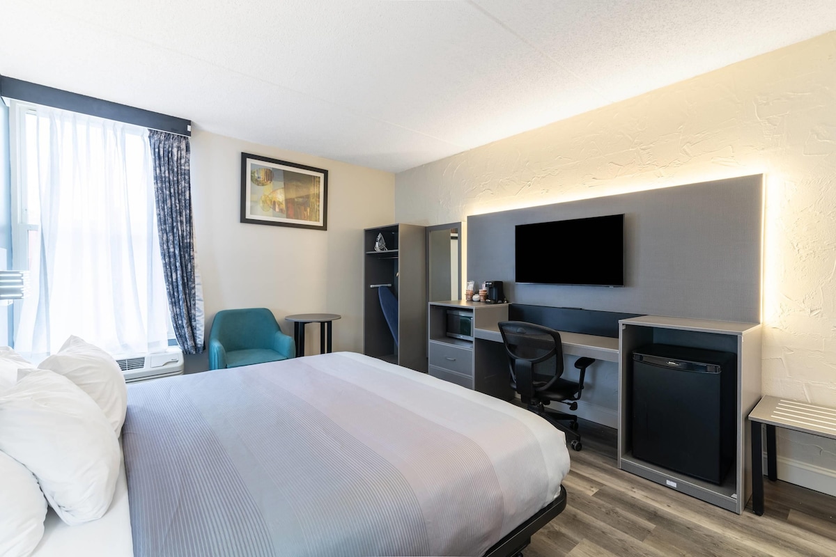 A hotel room with a bed, desk, chair, TV, and a small refrigerator.