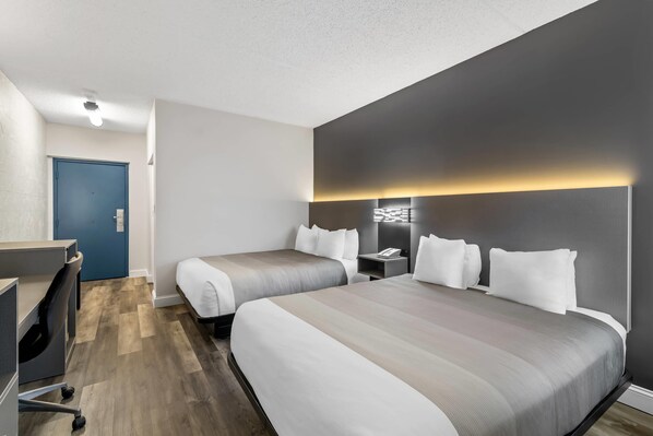 A hotel room with two beds, a desk, and a blue door.