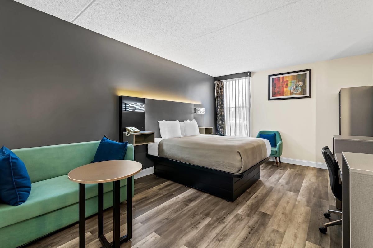 A hotel room with a bed, a green sofa, a small table, a desk, and a chair.