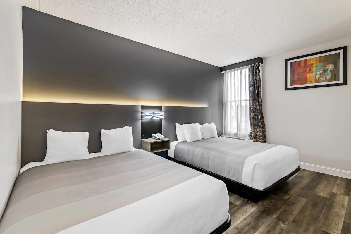 A hotel room with two beds, a nightstand, a wall-mounted light, and a painting.