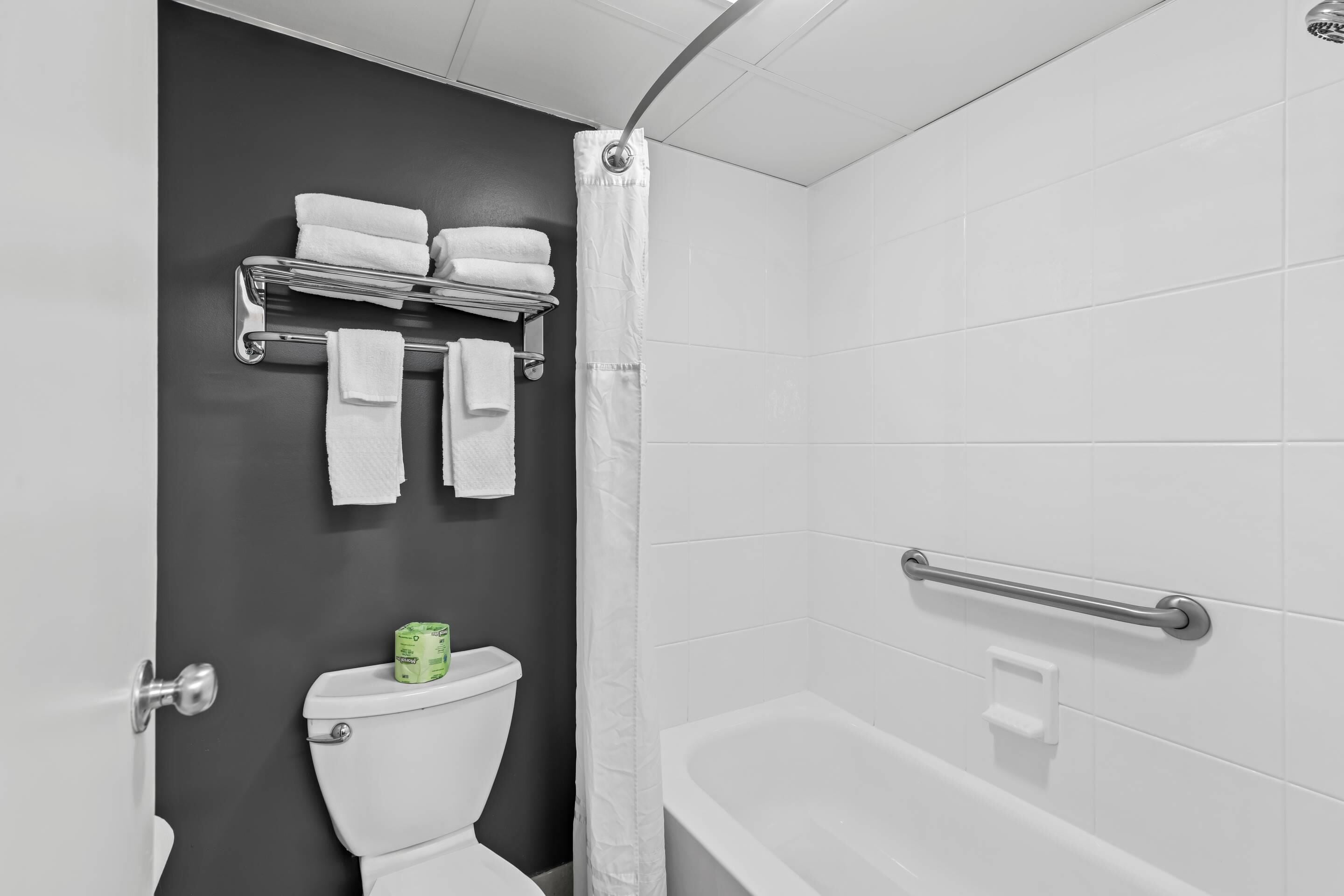 A bathroom with a toilet, a bathtub, a shower curtain, and a towel rack with folded towels.