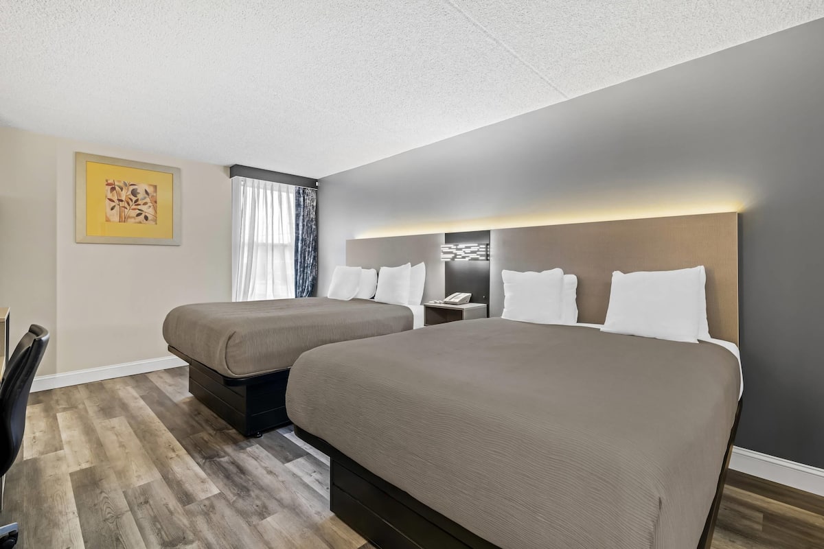 A hotel room with two beds, a desk, a chair, a nightstand, and a window with curtains.