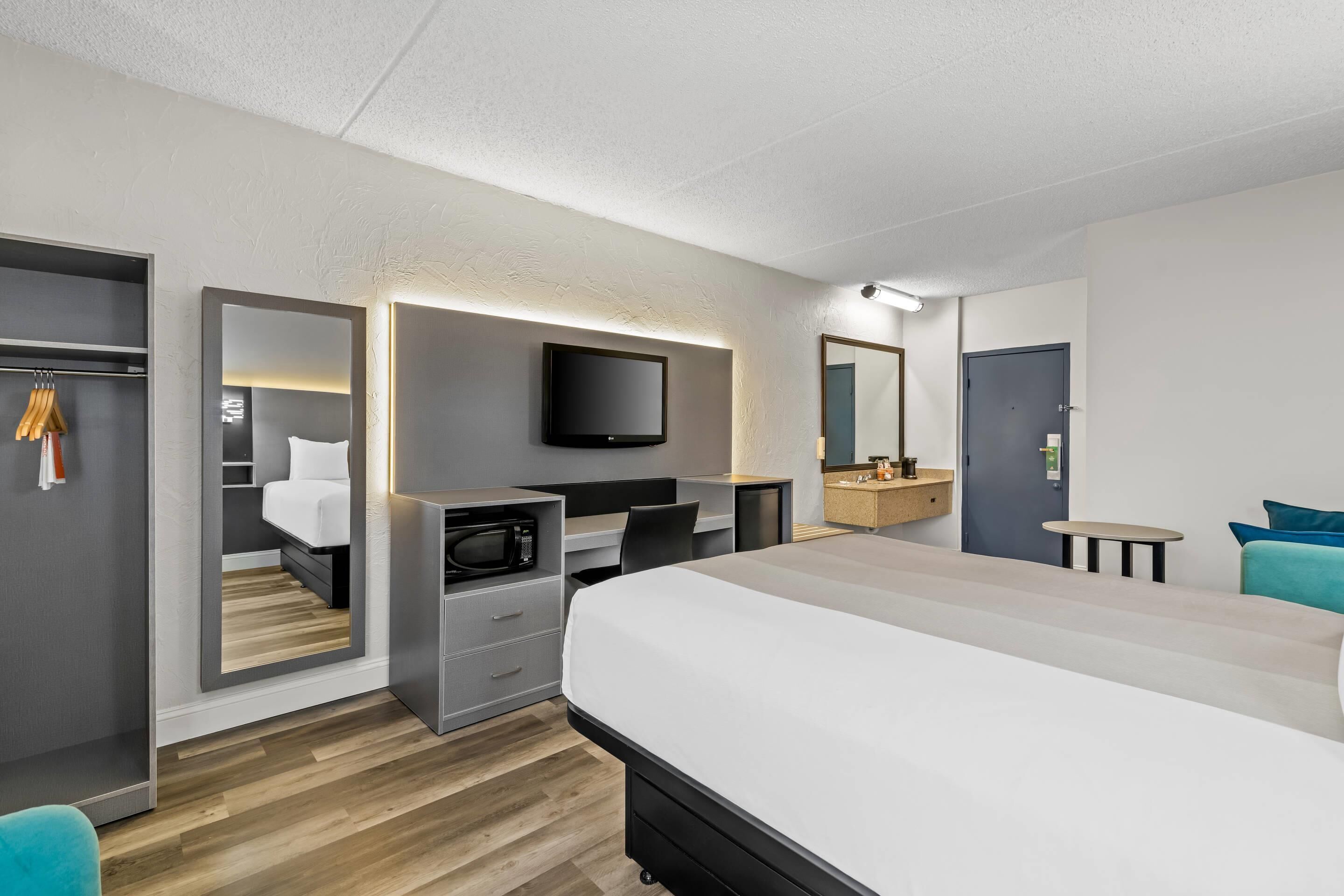 A modern hotel room with a large bed, a desk with a flat-screen TV, a microwave, and a wardrobe.