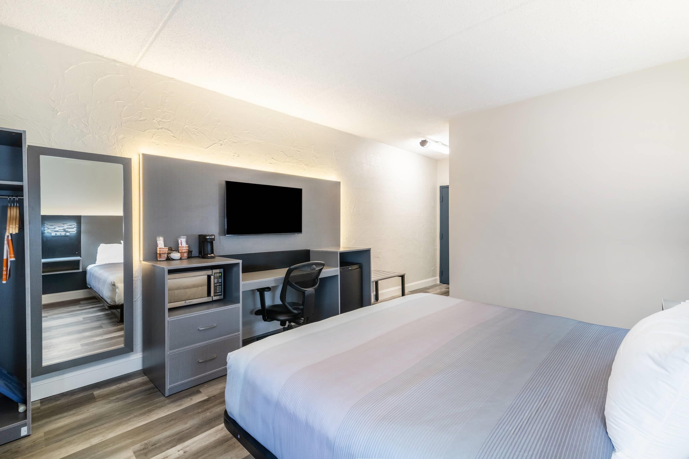 Una habitación de hotel moderna con una cama, un escritorio con silla, un televisor y un armario.