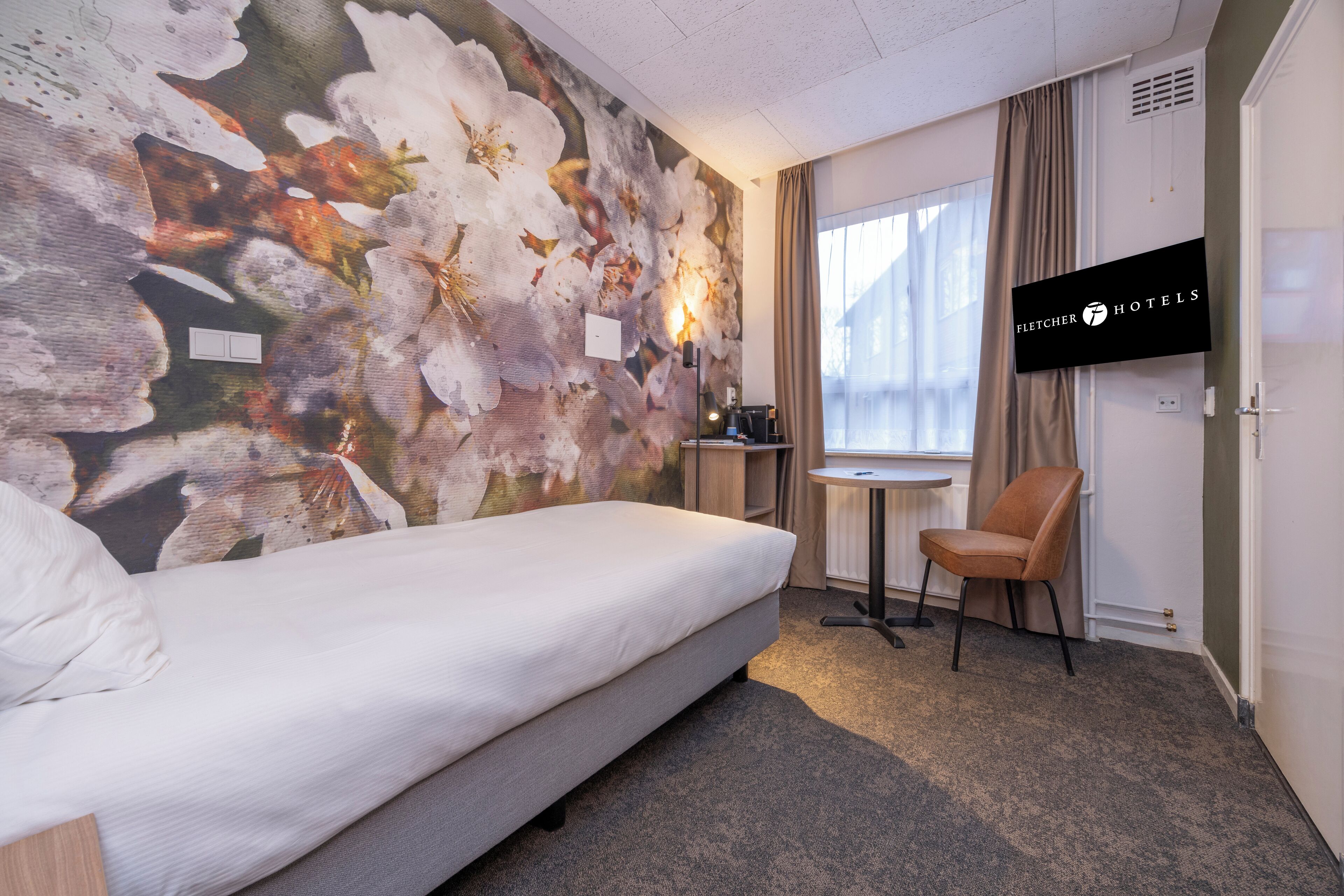 Habitación de hotel con cama, escritorio con silla, televisor y ventana con cortinas.