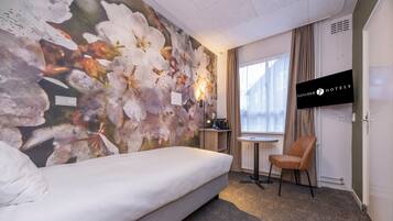 Une chambre d’hôtel comprenant un lit, un bureau avec une chaise, une télévision et une fenêtre avec des rideaux.