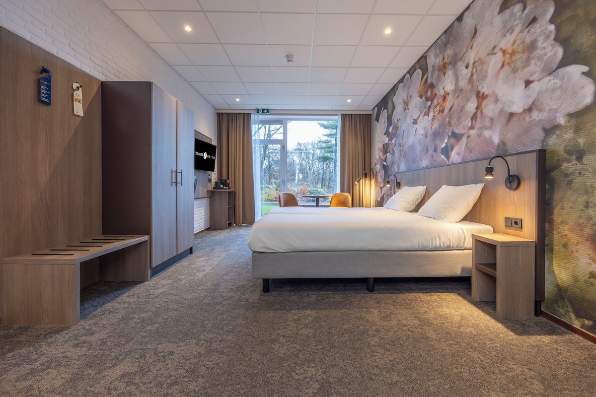 Ein Hotelzimmer mit einem Bett, einer Sitzbank, einem Schreibtisch und einem großen Fenster.