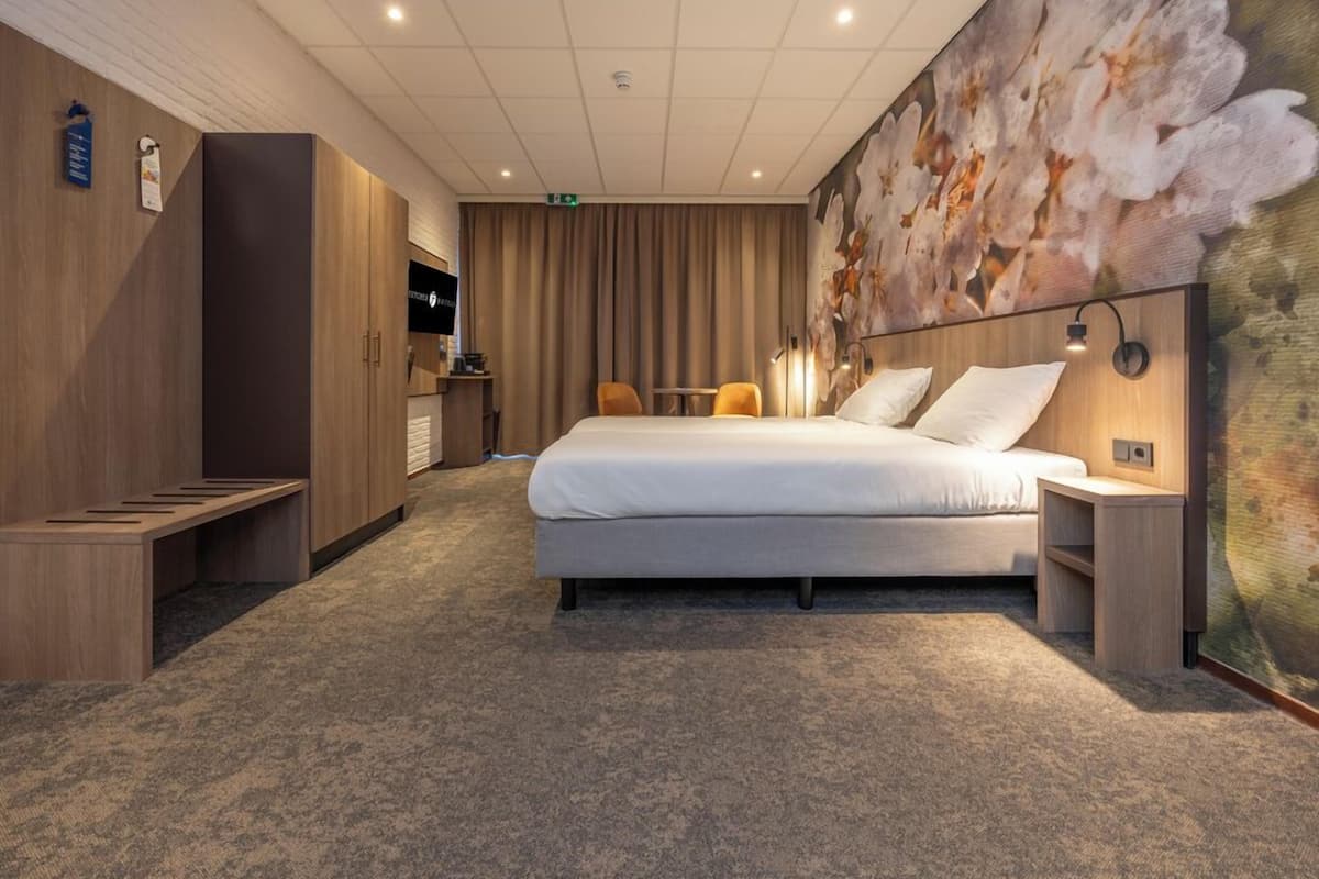 Ein Hotelzimmer mit einem großen Bett, einem Schreibtisch, einem Stuhl, einem Kleiderschrank und einem an der Wand befestigten Fernseher.