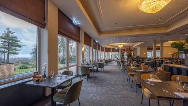 Un restaurante espacioso con amplios ventanales, una araña de cristal y mesas y sillas ordenadas.