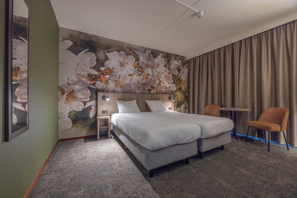 Ein Hotelzimmer mit einem großen Bett, einem Schreibtisch, einem Stuhl und einer Wand mit floralem Wandbild.