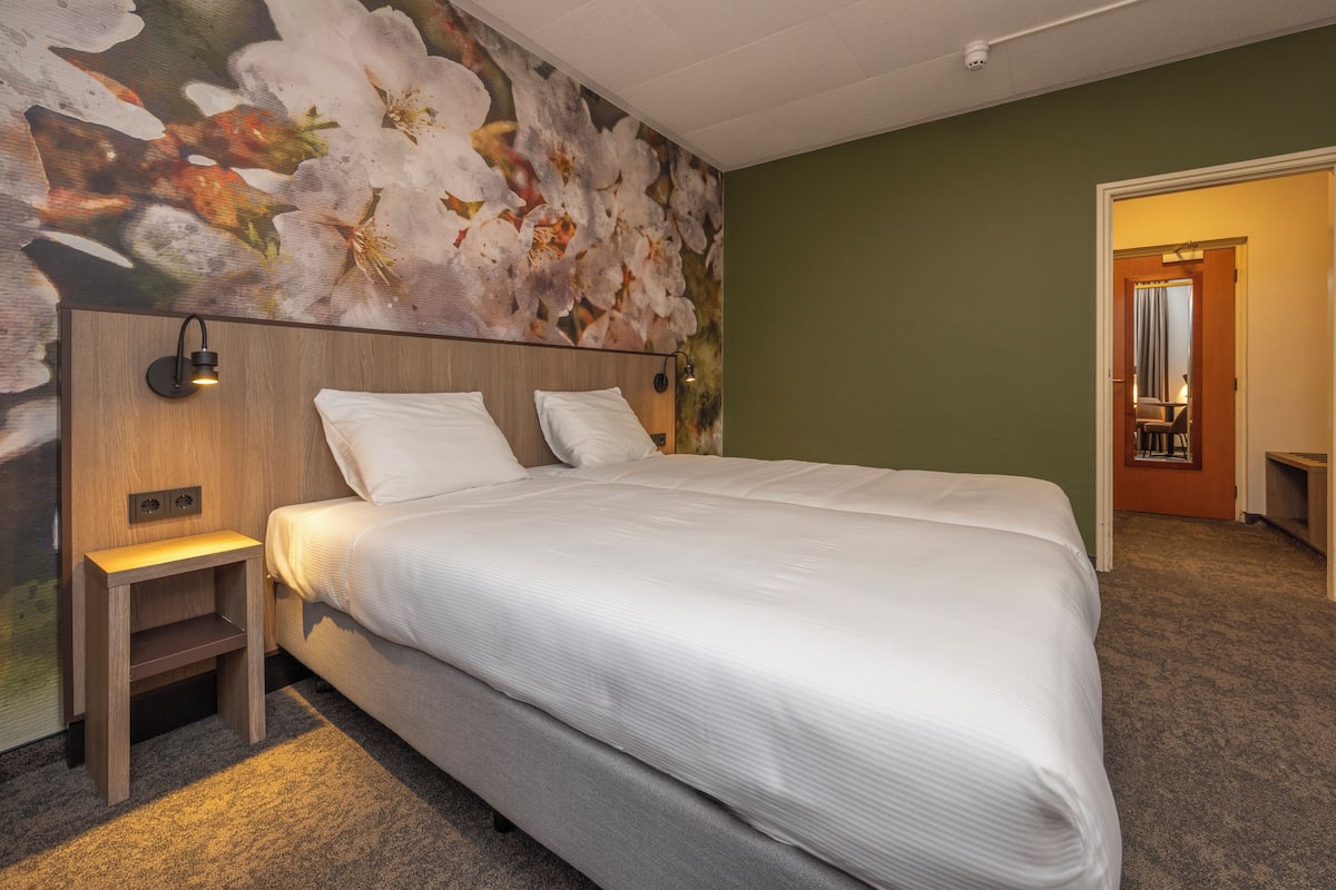 Ein Hotelzimmer mit einem großen Bett, einem Nachttisch, einer Wandleuchte und einem floralen Wandgemälde.