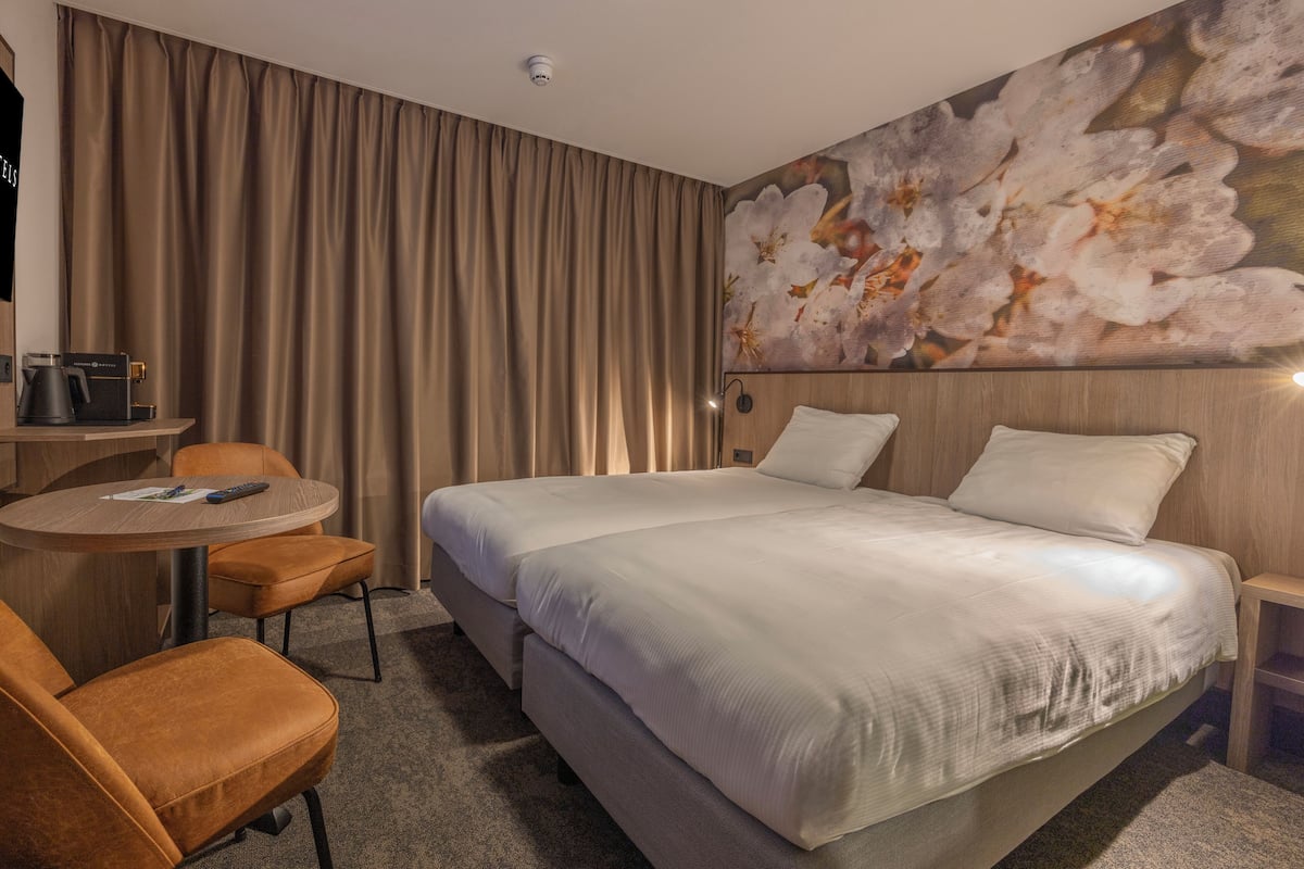 Ein Hotelzimmer mit einem großen Bett, einem runden Tisch mit Stuhl, einer Kaffeemaschine und einer Wandlampe.