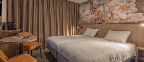 A hotel room with a large bed, a round table with a chair, a coffee maker, and a wall-mounted lamp.