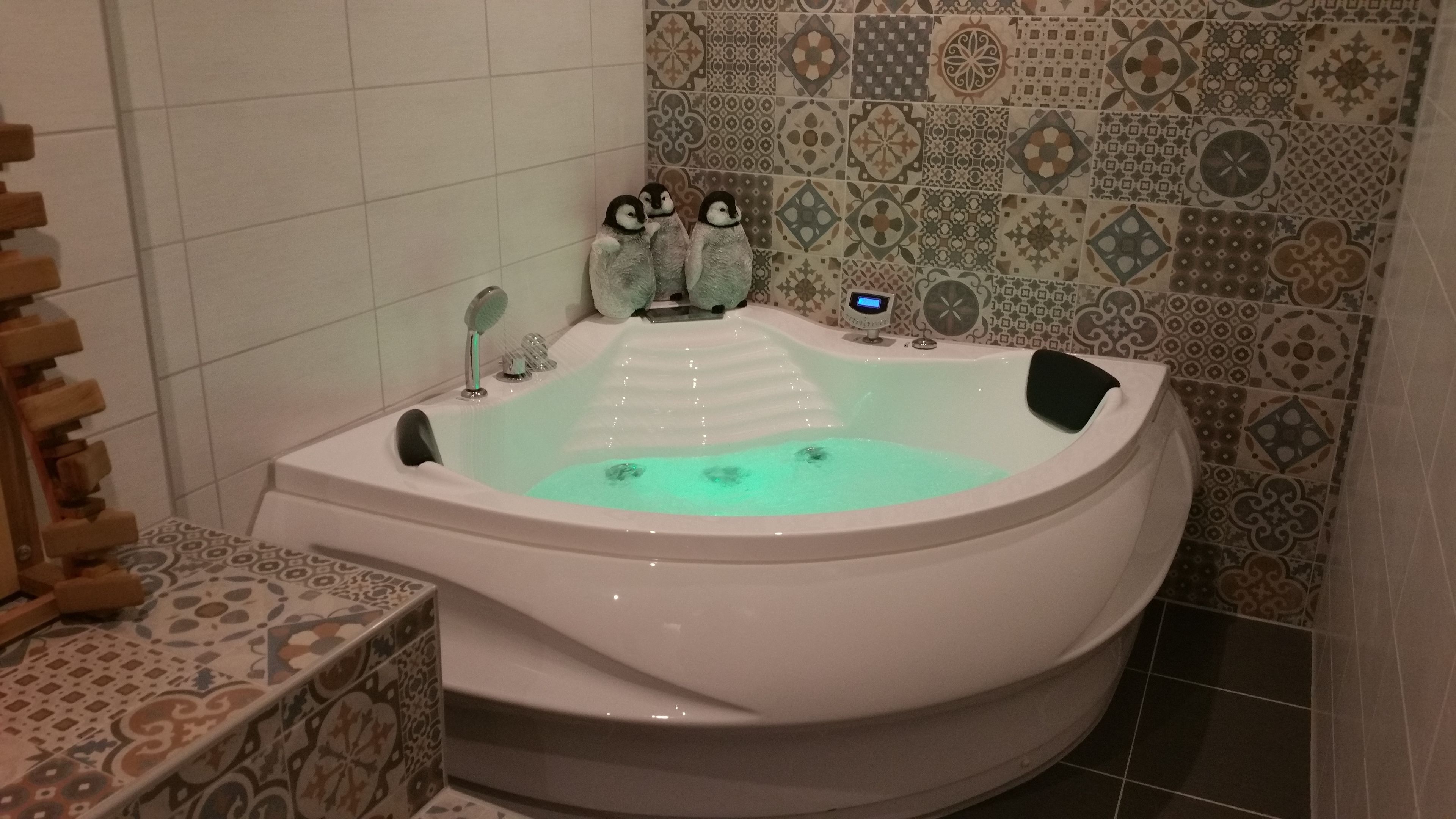 A modern bathroom with a freestanding bathtub, a wooden side table, and patterned tiles on the walls.