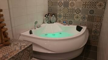 A modern bathroom with a freestanding bathtub, a wooden side table, and patterned tiles on the walls.