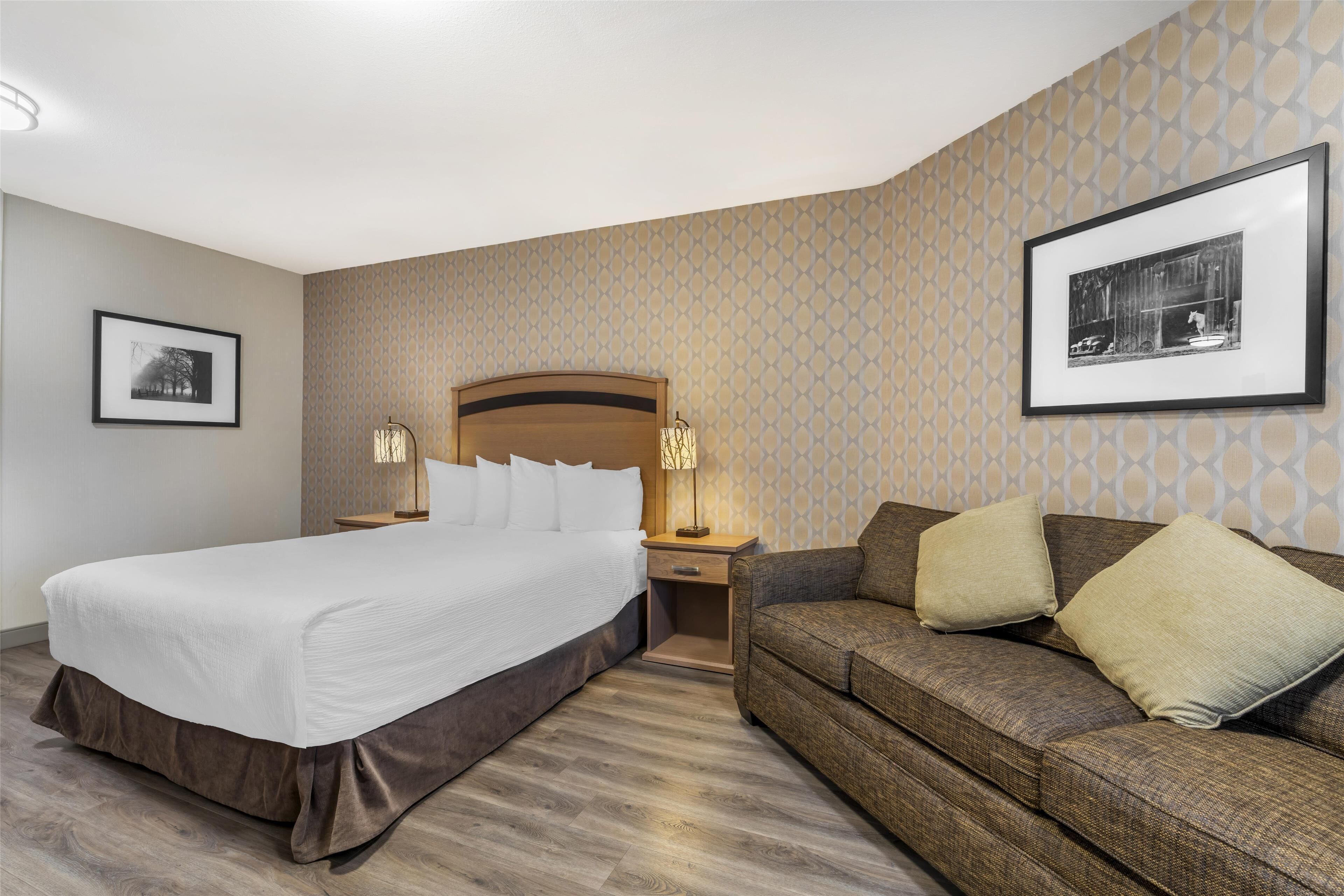 A hotel room with a large bed, a sofa, two bedside tables with lamps, and framed pictures on the walls.