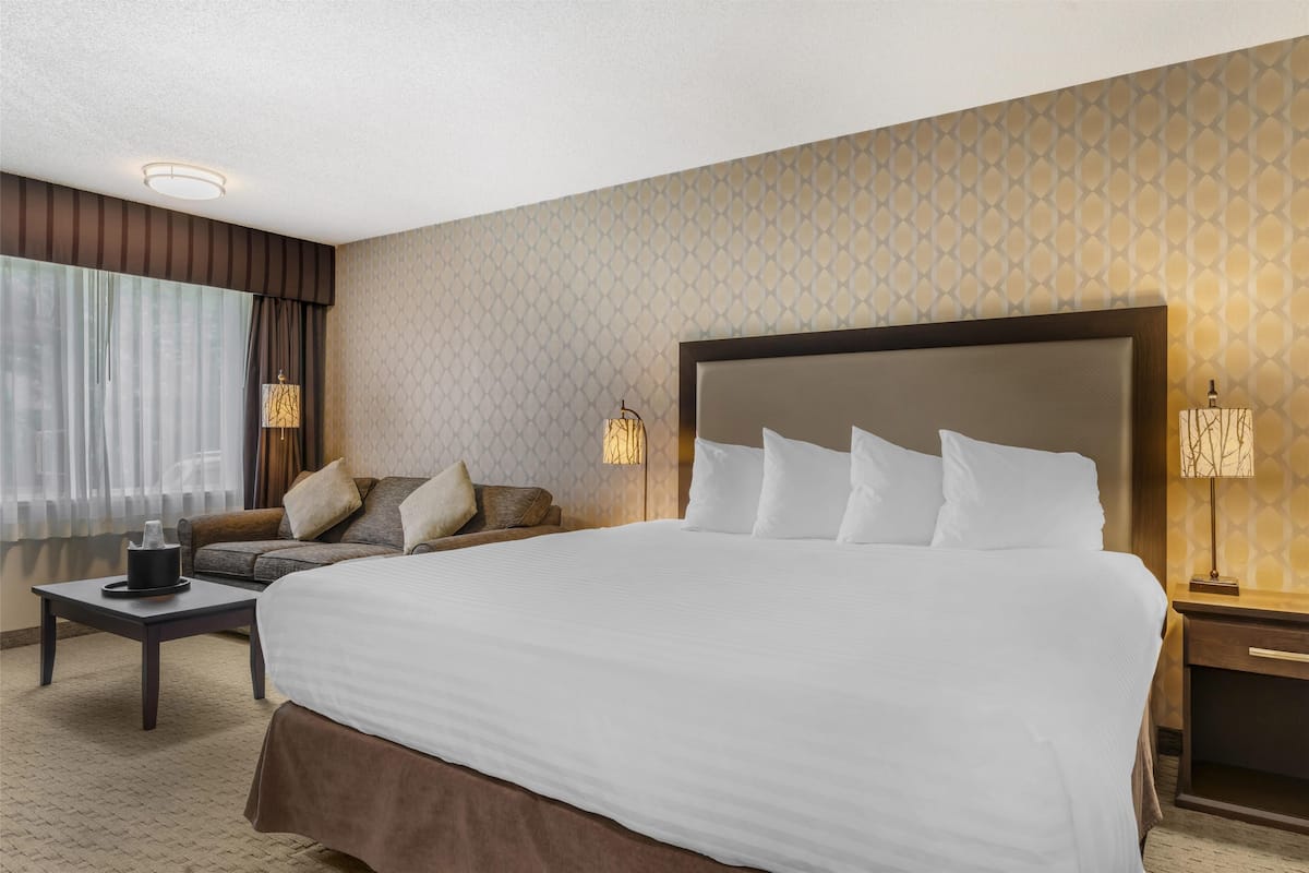 A hotel room with a large bed, a sofa, a small table, and two bedside lamps.