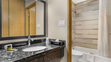 A bathroom with a granite countertop sink, a mirror, a toilet, and a shower area.