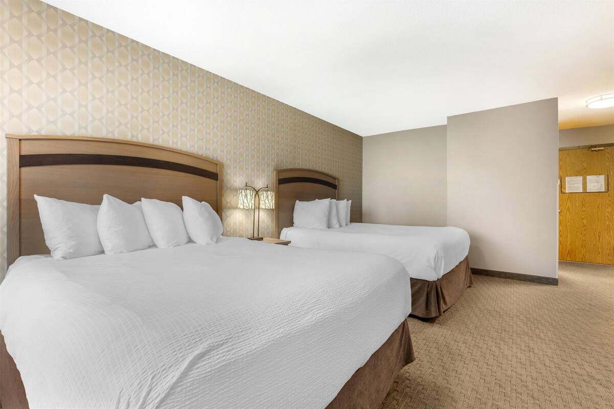 A hotel room with two beds, a wooden headboard, a patterned wall, and a carpeted floor.