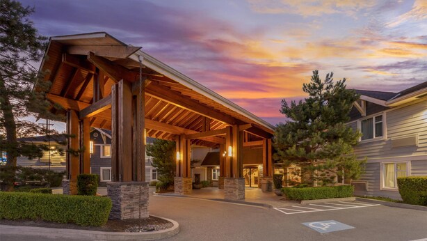 A hotel entrance with a covered patio, stone pillars, and a parking lot with handicapped accessibility. - Best Western Plus Country Meadows Inn (Langley)