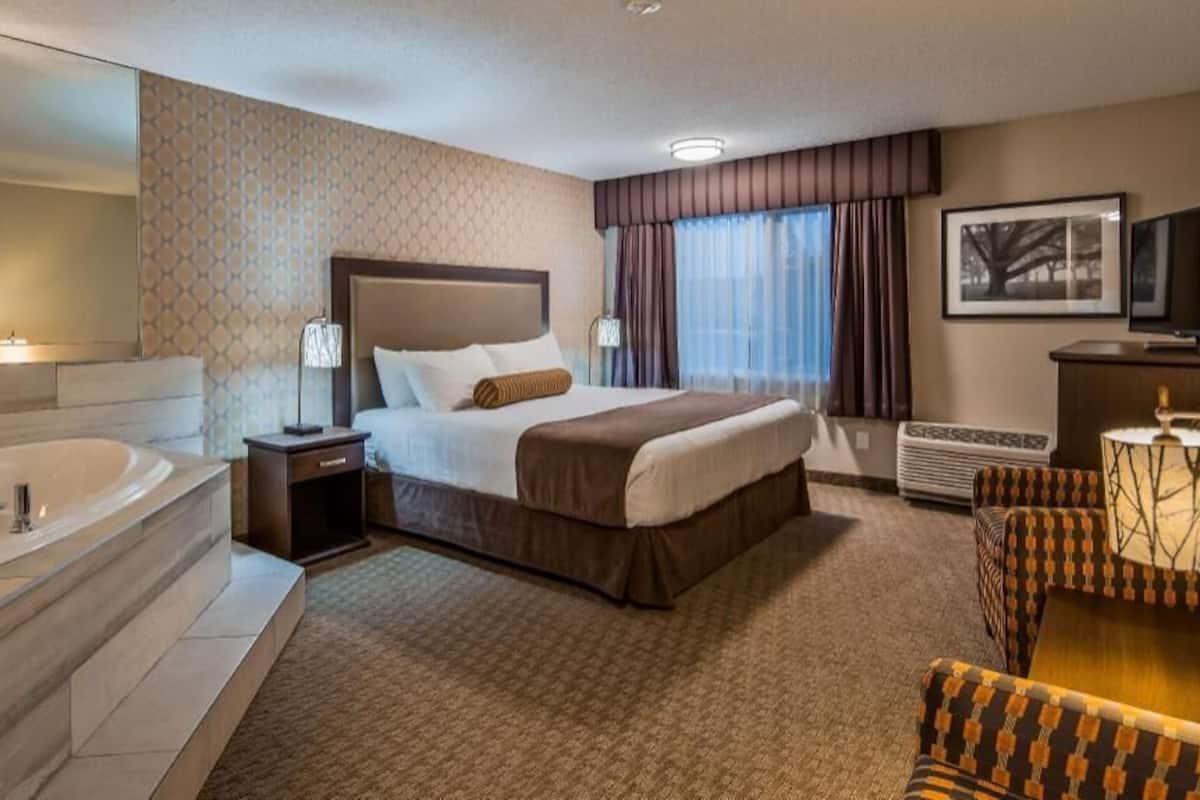A hotel room with a large bed, a separate bathroom with a bathtub, a desk with a television, and a patterned carpet.