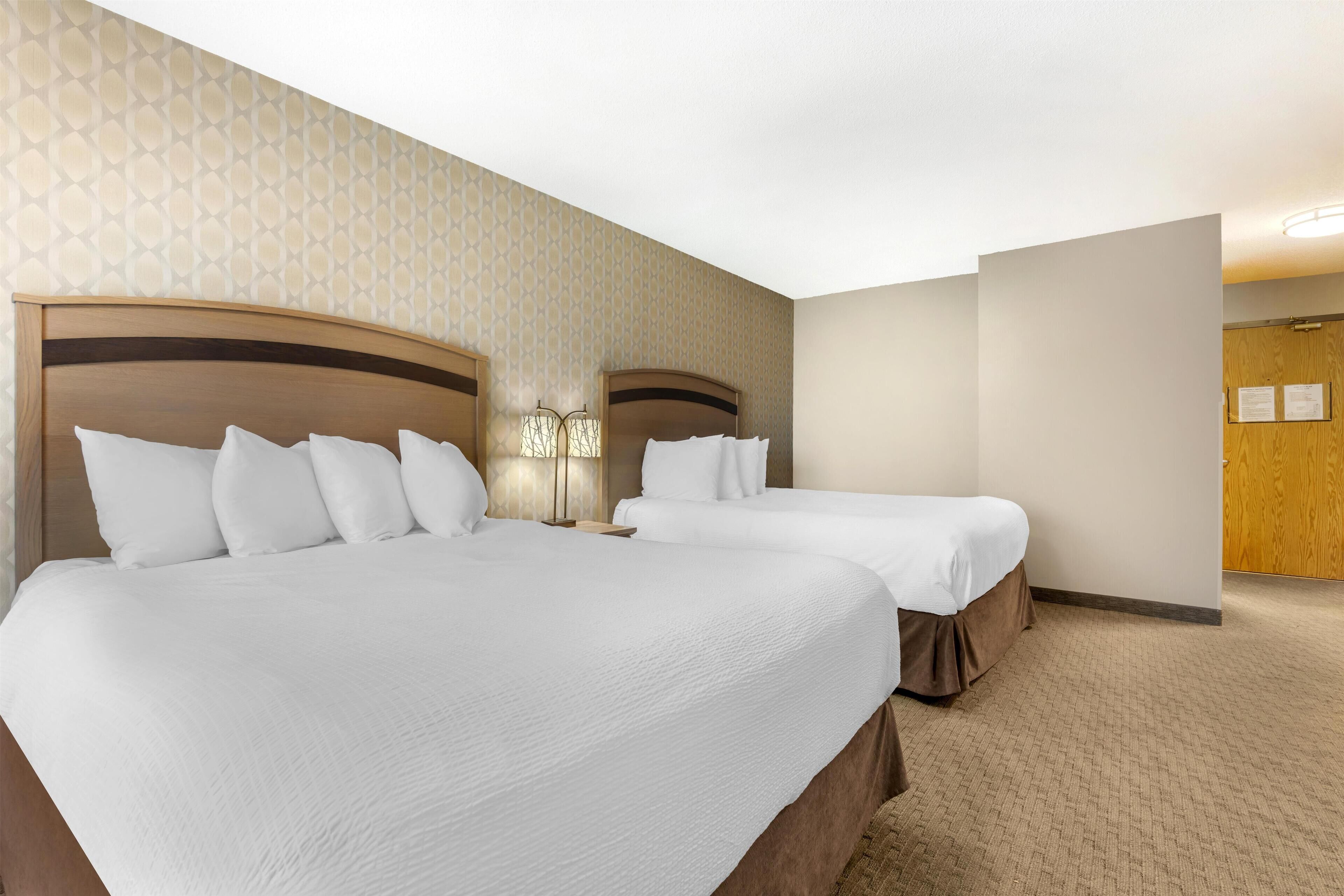 A hotel room with two beds, a patterned wallpaper, and a wooden door.