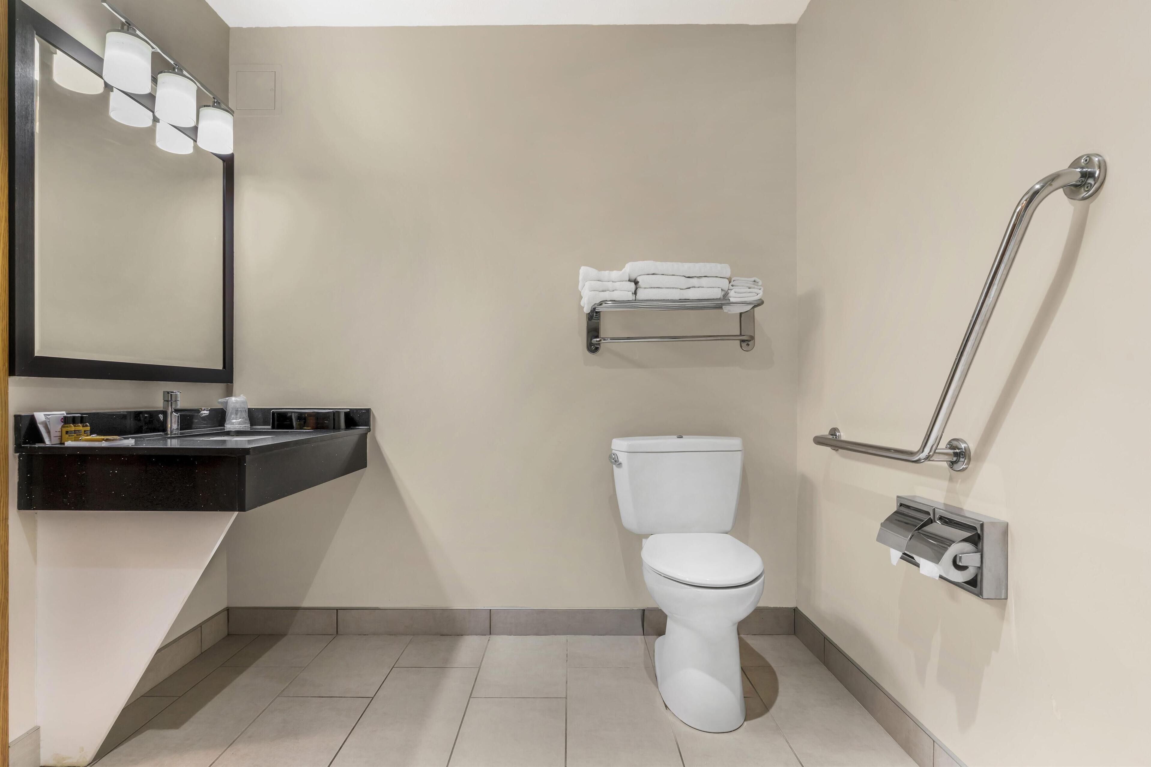 A modern bathroom with a white toilet, a black sink, a mirror with lights, a towel rack, and a grab bar.