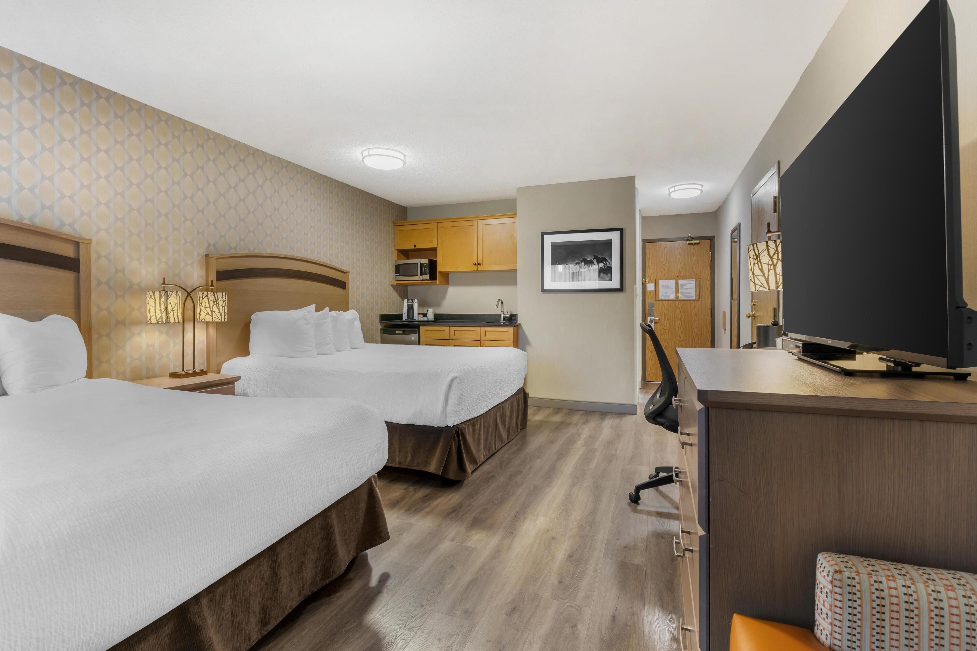 A hotel room with two beds, a desk, a TV, a microwave, and a small kitchenette.