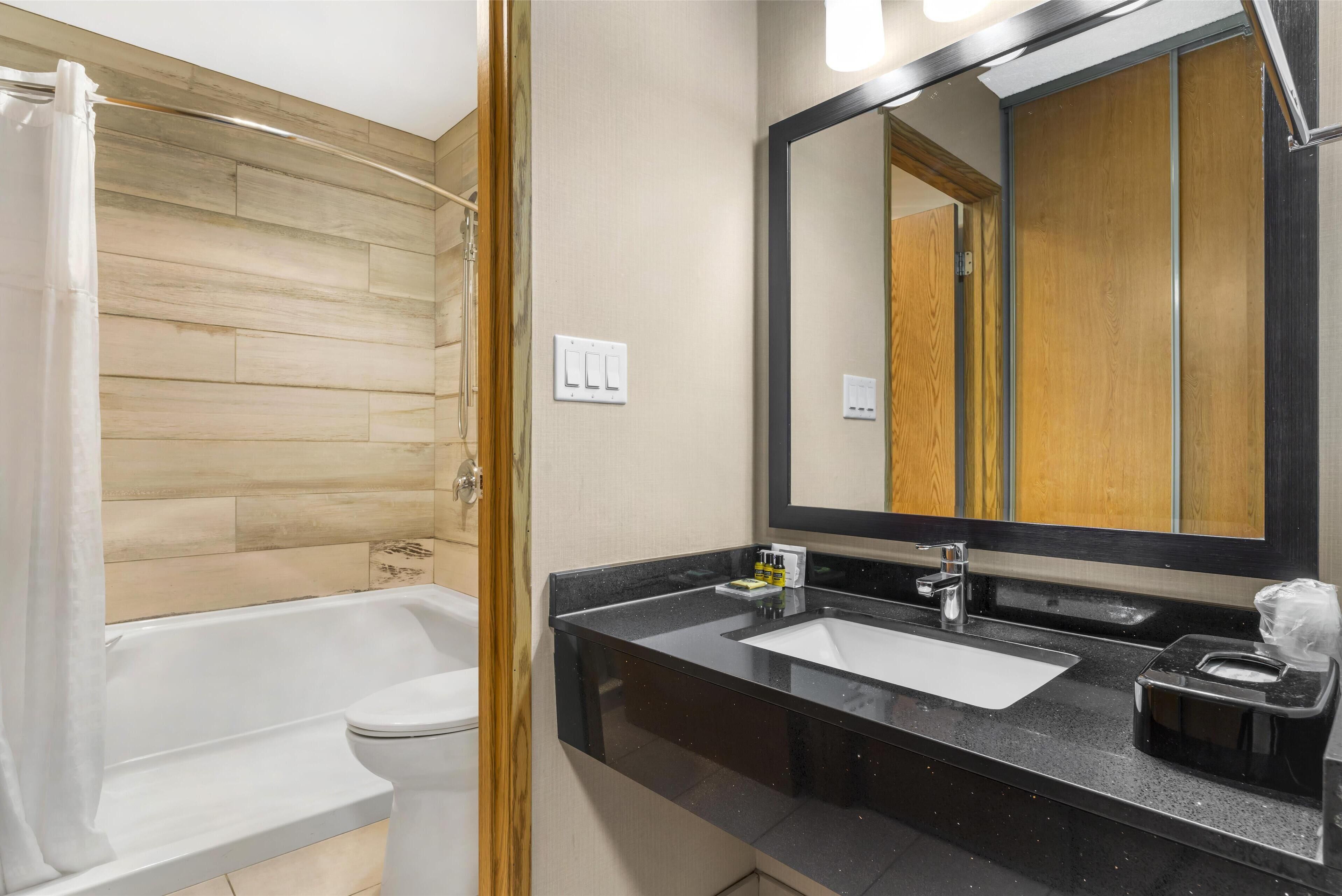 A modern bathroom with a wooden panel wall, a white bathtub, a sink with a black countertop, and a large mirror.