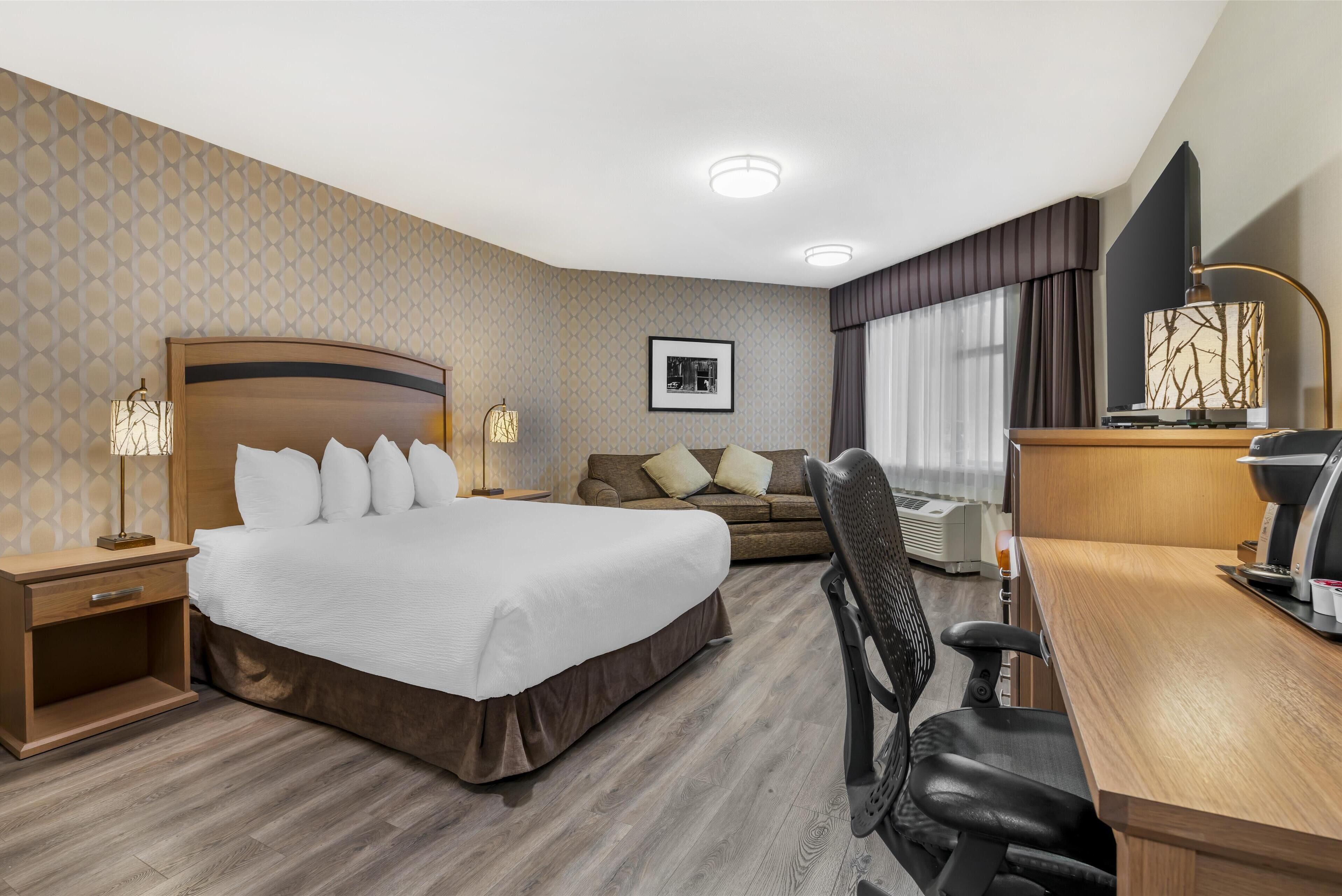 A hotel room with a large bed, a desk, a chair, a sofa, and a TV.