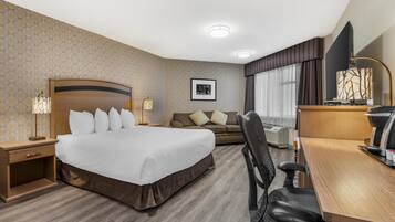 A hotel room with a large bed, a desk, a chair, a sofa, and a TV.