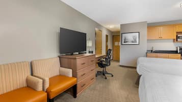 A hotel room with a bed, a desk with a chair, a television, a kitchenette, and a bathroom with a mirror.