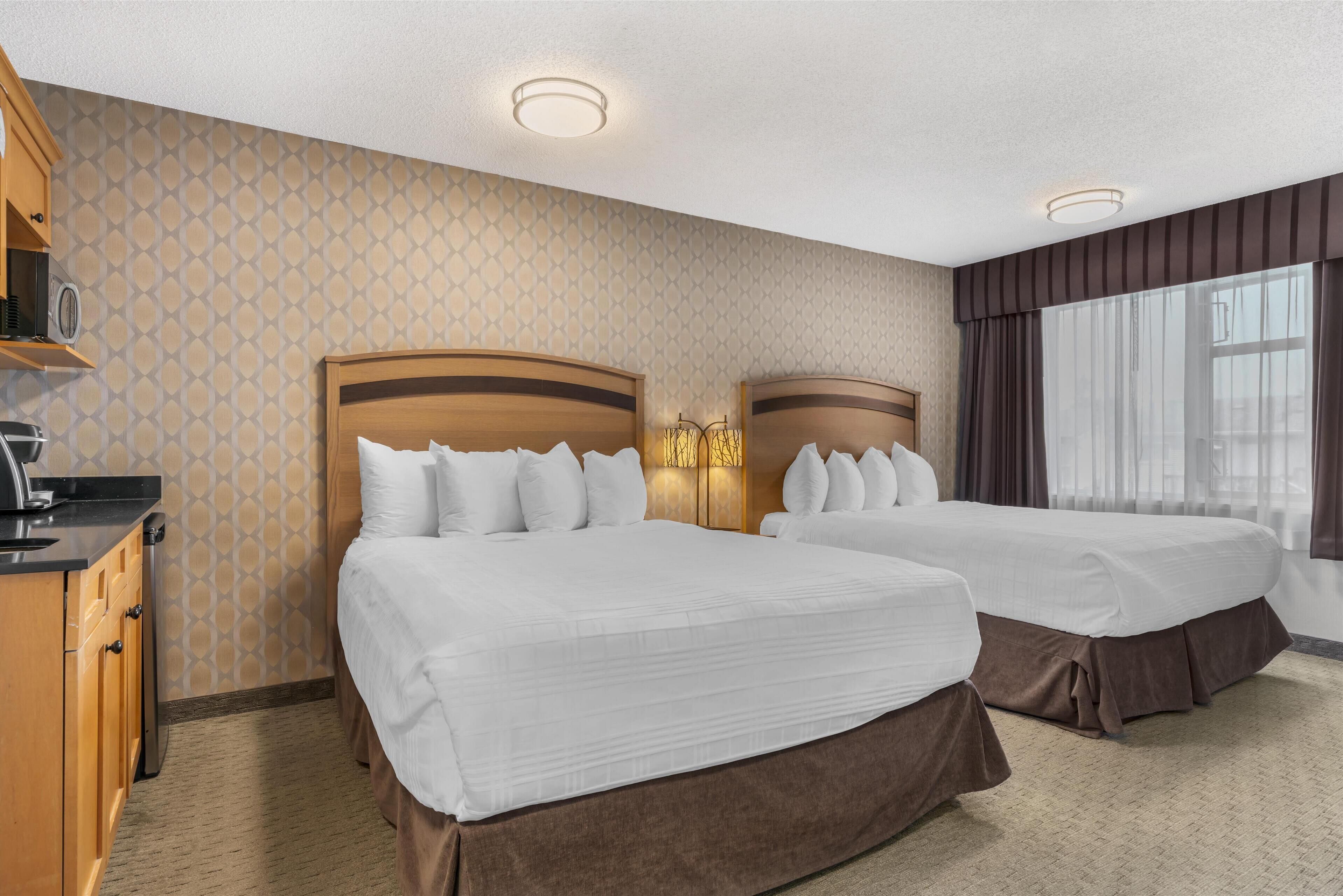 A hotel room with two beds, a minibar, and a large window with curtains.
