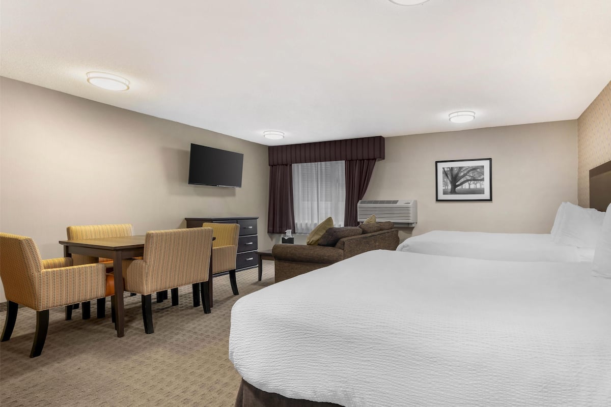 A hotel room with a large bed, a desk with chairs, a television, and a window with curtains.