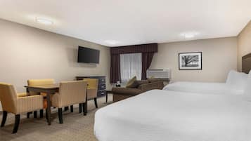 A hotel room with a large bed, a desk with chairs, a television, and a window with curtains.