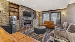 A modern living room with a stone accent wall, a flat-screen TV, a sofa, a coffee table, and a fireplace. - Best Western Plus Country Meadows Inn (Langley)
