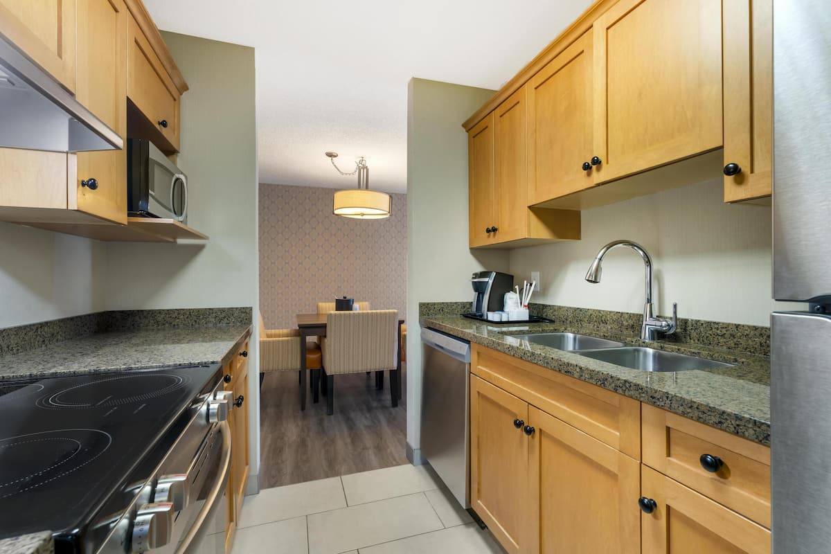 A modern kitchen with wooden cabinets, a stainless steel refrigerator, a built-in microwave, and a granite countertop.