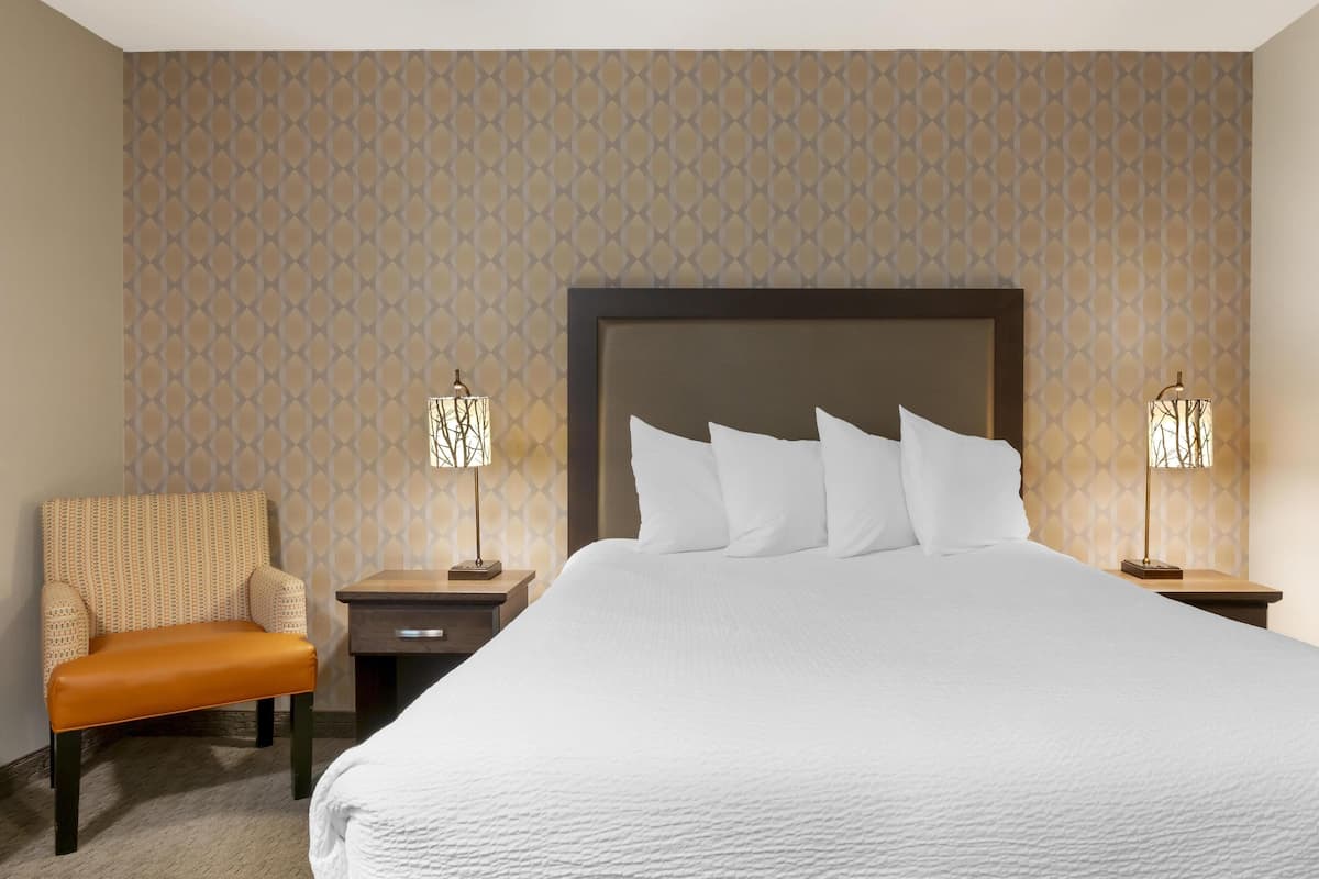 A hotel room with a large bed, two bedside tables, a chair, and patterned wallpaper.
