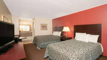 A hotel room with two beds, a TV, a desk, a lamp, and a bathroom with a mirror and lights.