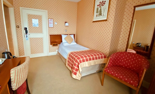 Quarto de hotel com cama, cadeira, escrivaninha e porta.