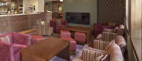 A spacious lounge area with striped sofas, a wooden coffee table, and a bar area in the background.