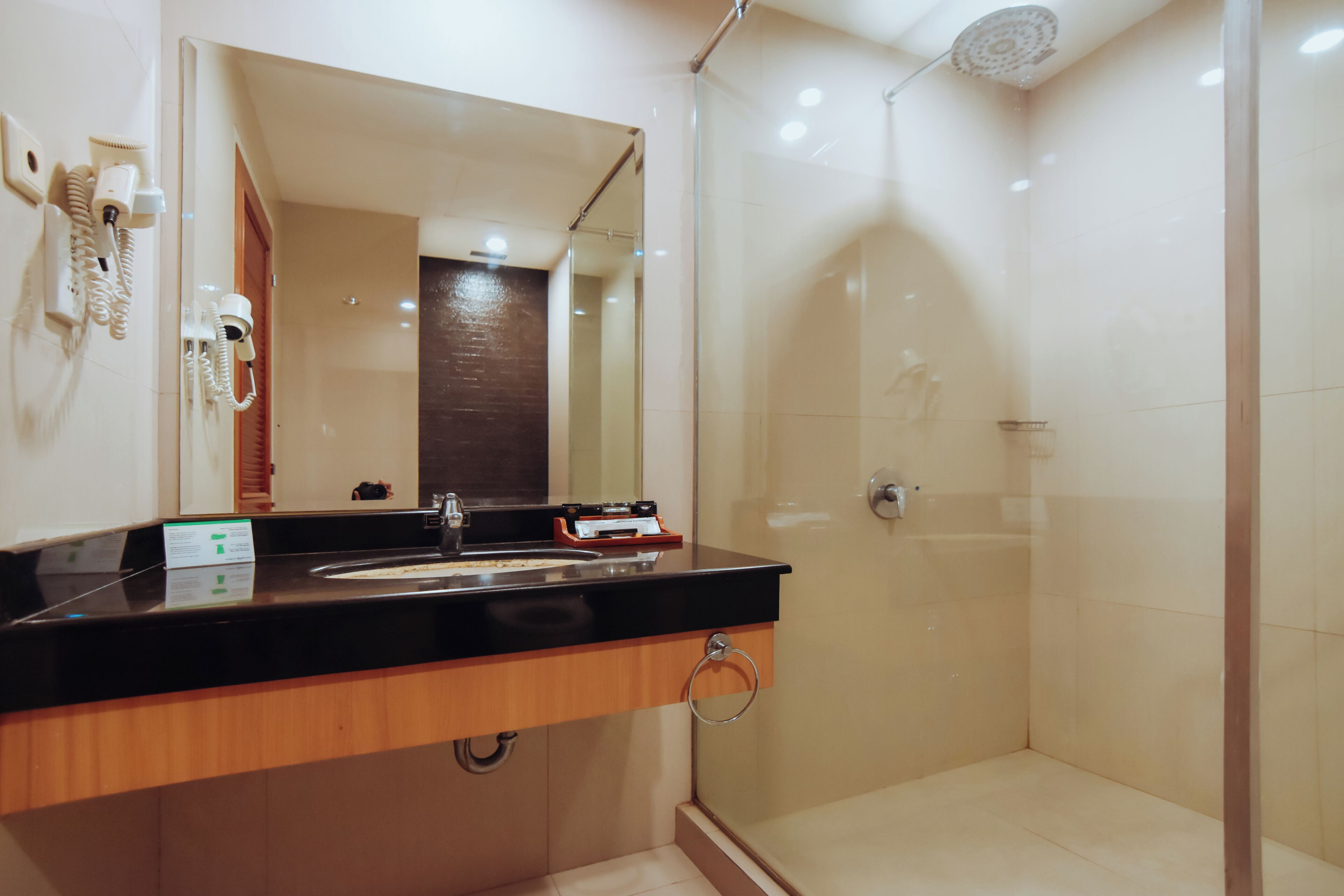 A modern bathroom with a black countertop, a mirror, a hairdryer, and a shower with a glass door.