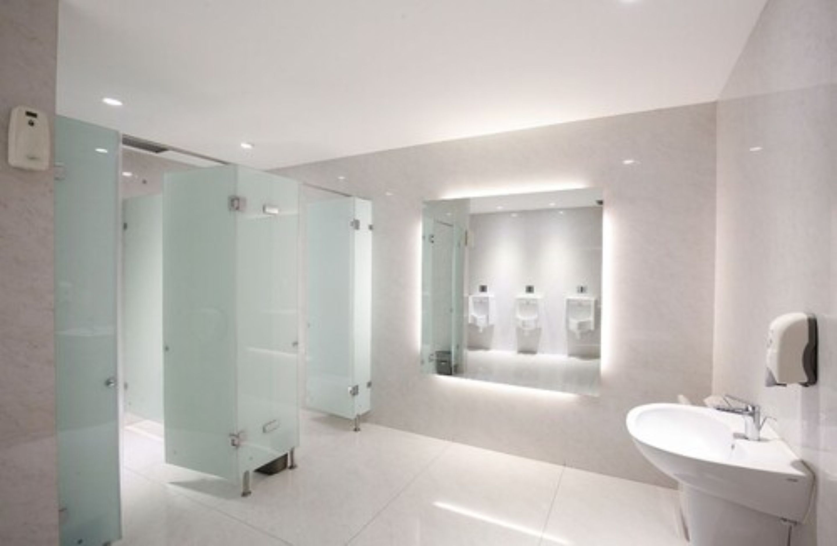 A modern bathroom with glass partitions, a sink, and hand dryers.