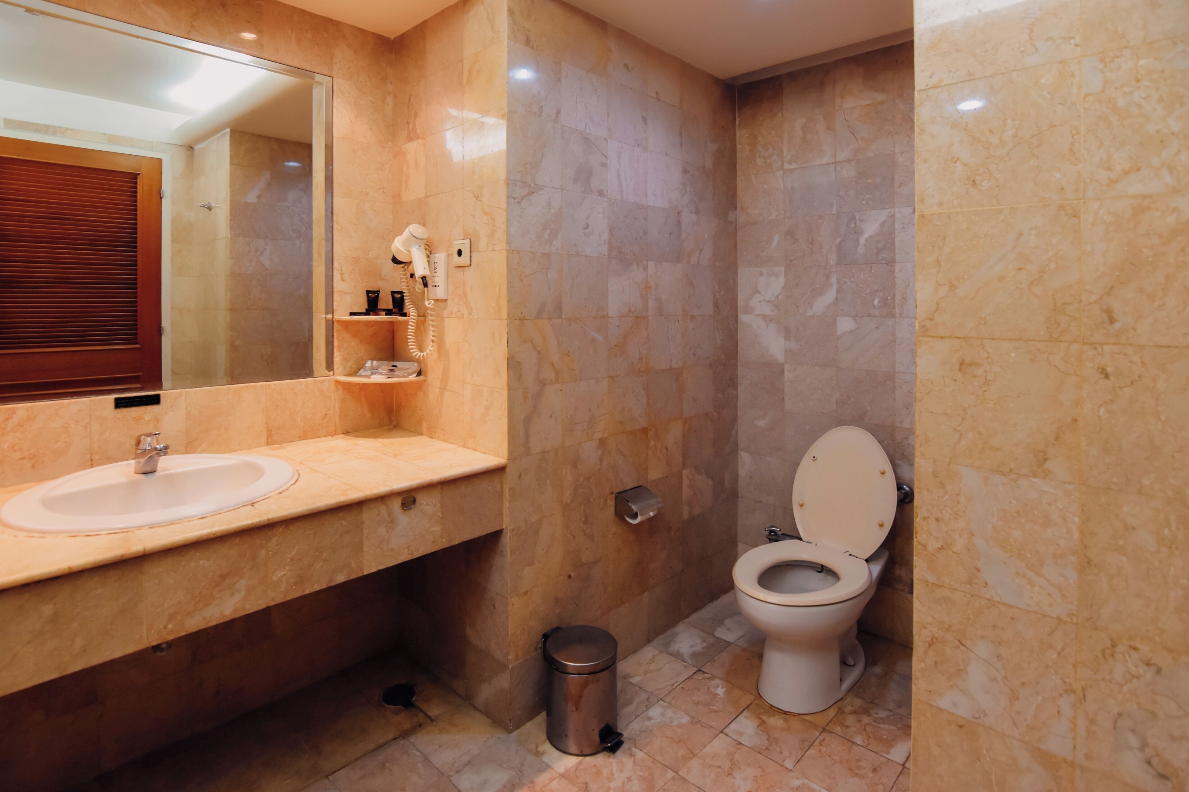 A modern bathroom with a marble sink, a toilet, and a hairdryer on the counter.