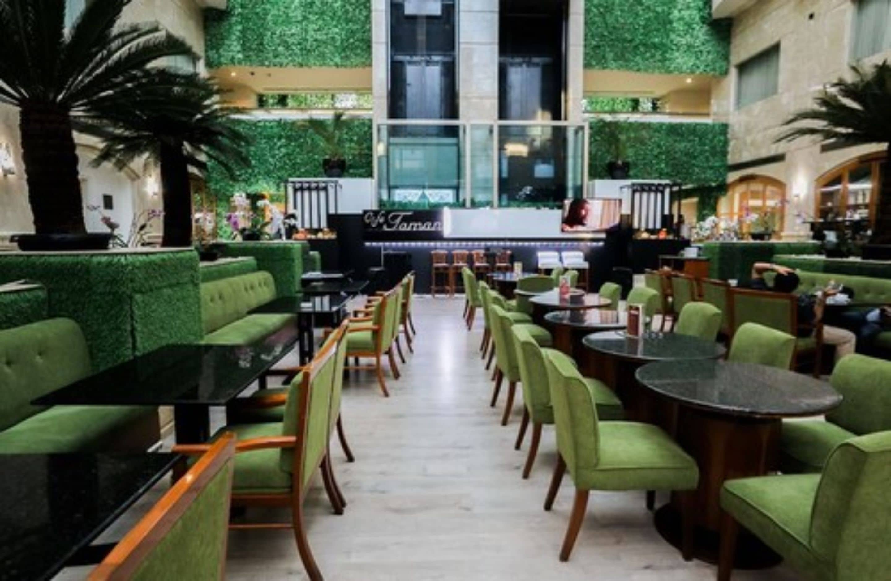 Un vaste espace intérieur doté de sièges et de tables recouverts d’un tissu vert, d’un bar central et offrant une vue sur l’extérieur grâce à de grandes fenêtres.
